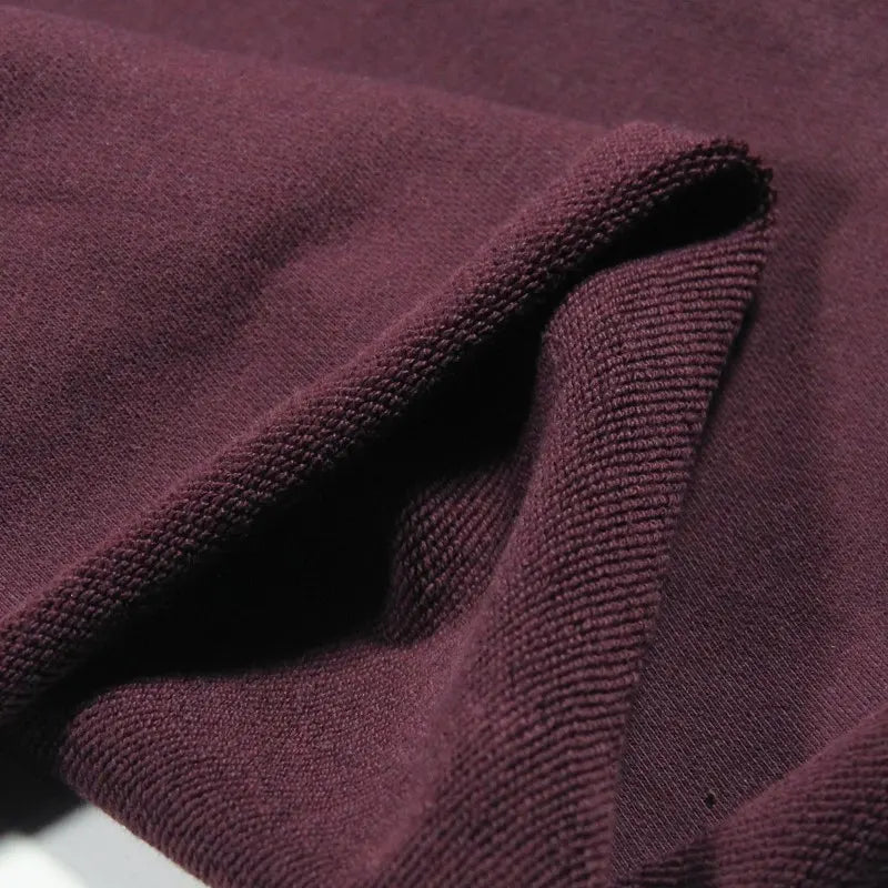 Gros plan sur le Tissu French Terry en coton uni au mètre de Longan Craft France, présenté en coloris bordeaux foncé, légèrement plié pour révéler son épaisseur, son tissage texturé et sa douceur idéale pour les sweat-shirts à capuche.