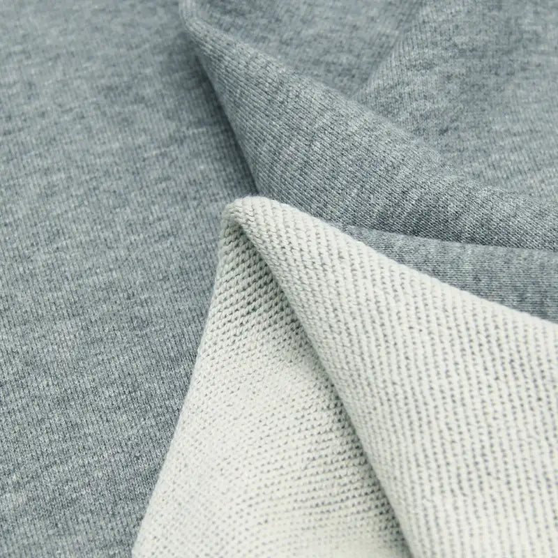 Gros plan sur deux couches : Tissu French Terry texturé gris clair de Longan Craft France et coton lisse gris moyen, plié en deux pour montrer les deux côtés. Tissu épais idéal pour les sweatshirts, disponible au mètre.
