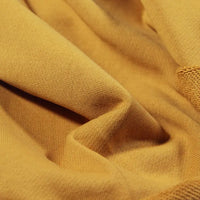 Gros plan sur le Tissu French Terry en coton uni au mètre de Longan Craft France en jaune moutarde, avec des plis doux et une texture légèrement nervurée et lisse-idéal pour sweat-shirts à capuche et vêtements confortables.
