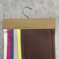 Un ensemble d'échantillons de denim lyocell de Longan Craft France - blanc, rose, bleu, jaune, marron - sont attachés à un cintre et présentés sur une surface grise. Ce tissu en lyocell sergé est respirant et confortable pour les jeans.