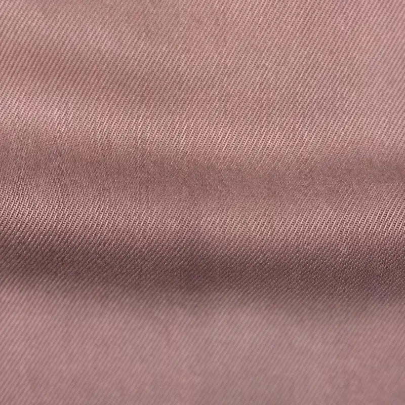 Gros plan sur le tissu en lyocell denim multicolore au mètre de Longan Craft France : un textile en lyocell sergé respirant et confortable, de couleur mauve clair, avec un tissage en diagonale qui présente des ombres subtiles et un léger pli, parfait comme tissu pour jeans.