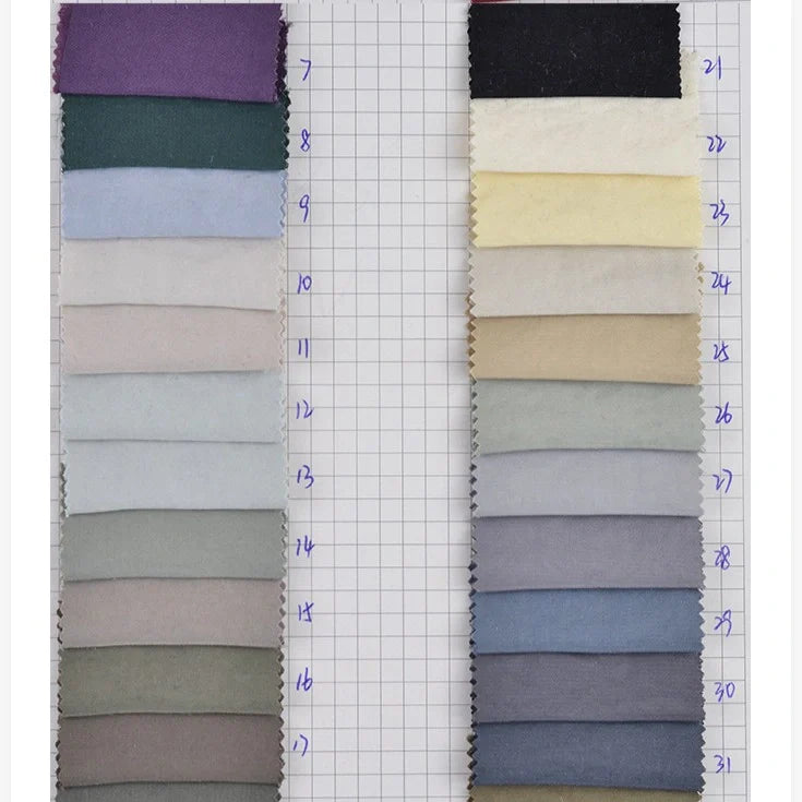Deux colonnes de Tissu peau de pêche uni double face au mètre de Longan Craft France, comprenant des échantillons de microfibres de polyester de différentes couleurs, sont disposées sur une grille avec les numéros 7-19 et 21-31 écrits à la main à côté de chaque échantillon de tissu.