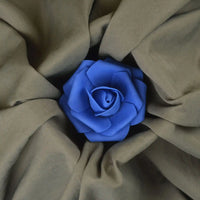 Une rose bleue trône au centre du tissu froissé Tissu peau de pêche uni double face de Longan Craft France. Les plis souples du tissu polyester microfibre marron clair rayonnent vers l'extérieur dans une présentation en forme de fleur.
