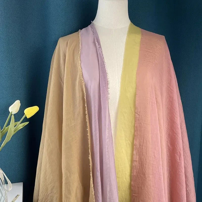 Un mannequin présente des panneaux de pêche pâle, de lavande, de jaune et de rose en Tissu lin et soie uni de Longan Craft France. Deux tulipes blanches et jaunes reposent en bas à gauche sur un fond sarcelle foncé.