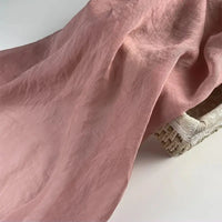 Un morceau de tissu lin et soie uni au mètre de Longan Craft France, un fin mélange de lin, de lyocell et de soie idéal pour l'ameublement, est drapé sur un panier beige tissé, montrant sa texture douce et ses plis délicats.