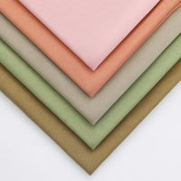 Cinq pièces de Jersey modal uni au mètre de Longan Craft France, en rose, pêche, beige, vert clair et vert olive, sont soigneusement disposées en éventail. Ce tissu jersey coton-modal est idéal pour les doux vêtements de nuit pour enfants.
