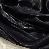 Gros plan sur l'organza noir et brillant de Longan Craft France, drapé en plis lâches et reflétant la lumière. Le tissu organza lisse et transparent uni au mètre contraste avec une surface texturée blanche dans le coin inférieur gauche.