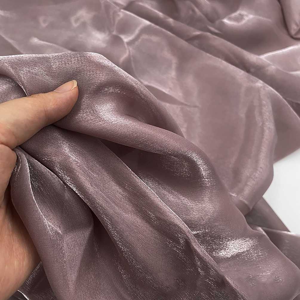Une main tient Tissu organza uni au mètre de Longan Craft France, un organza transparent mauve clair avec une finition lisse et brillante, idéal pour les vêtements et la décoration.