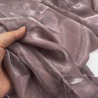 Une main tient Tissu organza uni au mètre de Longan Craft France, un organza transparent mauve clair avec une finition lisse et brillante, idéal pour les vêtements et la décoration.