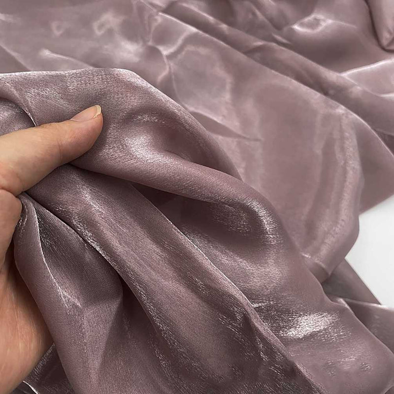 Une main tient Tissu organza uni au mètre de Longan Craft France, un organza transparent mauve clair avec une finition lisse et brillante, idéal pour les vêtements et la décoration.