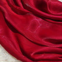 Gros plan sur un tissu rouge Tissu organza uni au mètre de Longan Craft France, un tissu léger et transparent idéal pour les vêtements et la décoration, montrant des plis brillants sur une surface texturée blanche.