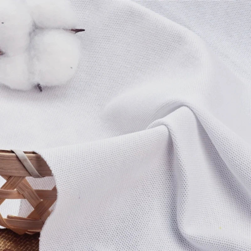 Gros plan sur le Tissu piqué uni au mètre-coton-polyester pour polos de Longan Craft France, drapé sur un panier avec une balle de coton, mettant en valeur le tissage distinctif et la finition lisse du tissu, idéal pour les chemises et les polos d'été DIY.
