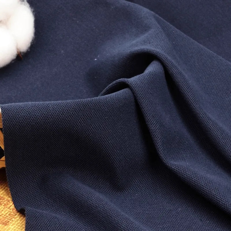 Gros plan sur le tissu piqué uni au mètre de Longan Craft France, un tissu coton-polyester bleu marine foncé à la surface texturée, présenté plié à côté d'un coton brut - un tissu idéal pour les polos d'été et les chemises à manches courtes.