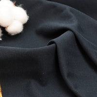 Gros plan sur le tissu piqué uni au mètre bleu foncé de Longan Craft France, plié en douceur à côté de rouleaux de coton blanc - un tissu idéal en coton-polyester pour les polos et les chemises à manches courtes de l'été.