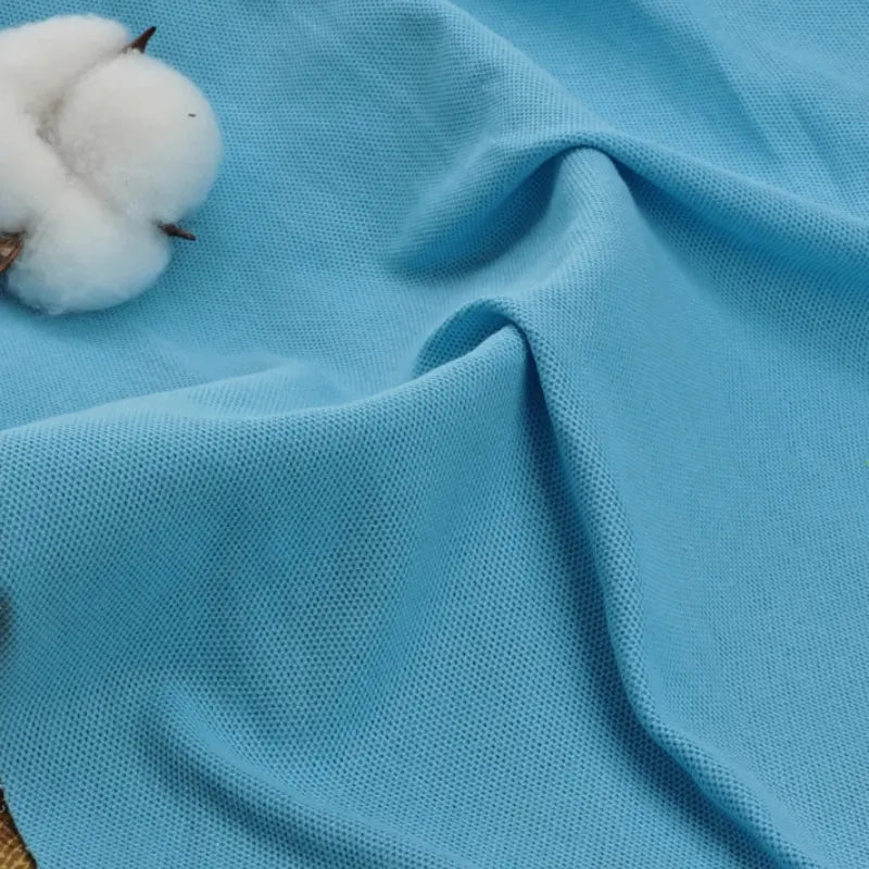 Un gros plan sur le Tissu piqué uni au mètre bleu clair de Longan Craft France montre son mélange doux et texturé de coton et de polyester, idéal pour les polos et les chemises d'été, avec des boules de coton qui soulignent sa qualité respirante.