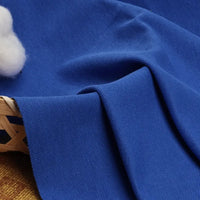 Gros plan sur le tissu piqué uni au mètre - un mélange coton-polyester idéal pour chemises ou polos d'été - de Longan Craft France, drapé sur un panier, avec du coton blanc à proximité sur une surface à motifs marron et or.