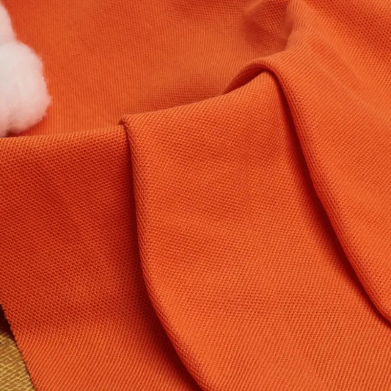 Gros plan sur le Tissu piqué uni au mètre orange de Longan Craft France, idéal pour les polos et les chemises d'été. Un petit morceau de coton blanc est visible en haut à gauche. Tissu coton-polyester parfait pour les projets de bricolage.