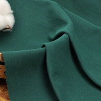 Un gros plan de Longan Craft France tissu piqué uni au mètre, coton-polyester pour polos, présente sa texture drapée sur un panier en osier, avec une fleur de coton visible dans le coin supérieur gauche.