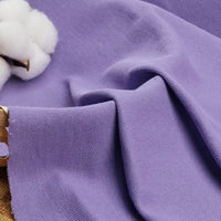 Un échantillon de Tissu piqué uni au mètre de Longan Craft France, un mélange de coton et de polyester idéal pour les polos et les chemises d'été, est drapé sur une surface à côté d'une balle de coton, mettant en valeur son tissage texturé et sa douceur.