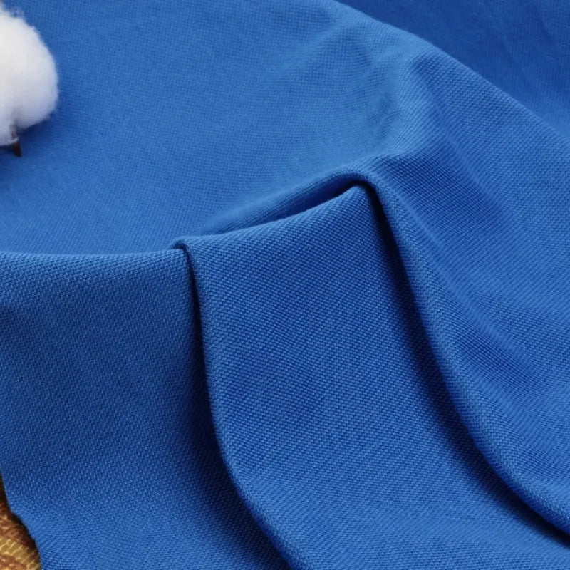 Gros plan sur le tissu bleu piqué uni au mètre de Longan Craft France, un tissu coton-polyester idéal pour les chemises et les polos d'été ; le coton blanc apparaît dans le coin supérieur gauche.