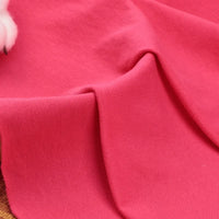 Un gros plan du tissu piqué uni au mètre rose vif de Longan Craft France montre son tissage doux et texturé en coton-polyester avec des plis visibles. Une partie d'un objet blanc apparaît dans le coin supérieur gauche. Parfait pour les chemises et polos d'été DIY.