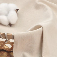 Gros plan sur le tissu piqué uni au mètre beige de Longan Craft France, un tissu coton-polyester pour polos et chemises d'été DIY, drapé sur un panier avec du coton brut reposant sur sa surface texturée.