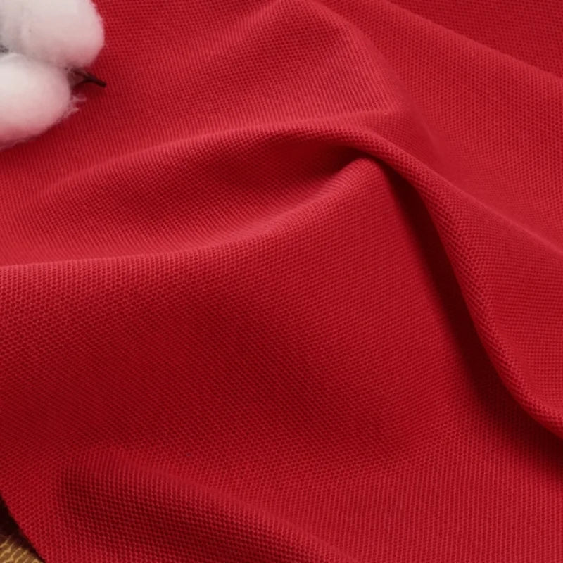 Gros plan sur le tissu piqué rouge coton-polyester de Longan Craft France pour les chemises et polos d'été, montrant sa texture et ses plis souples, avec une partie d'une balle de coton dans le coin supérieur gauche.