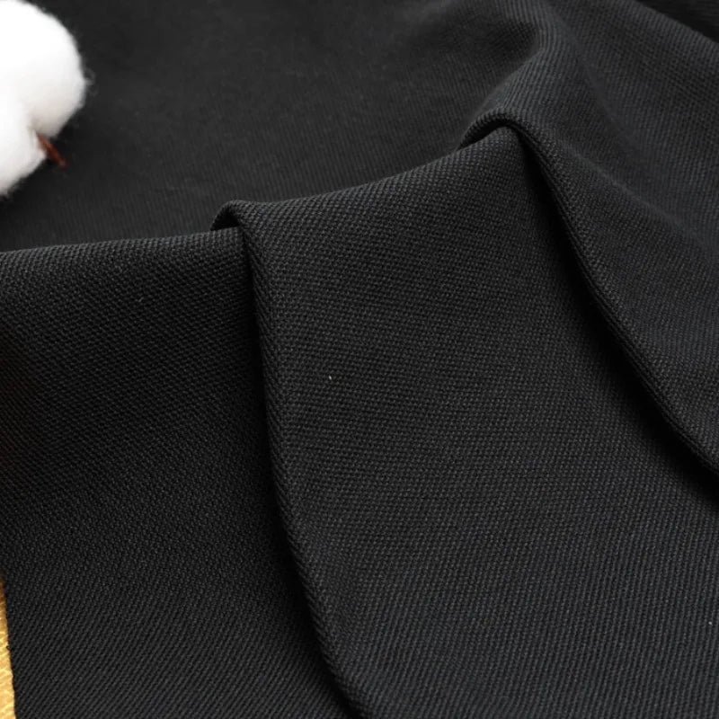 Gros plan sur le tissu noir piqué uni au mètre plié de Longan Craft France, qui présente une surface lisse et texturée en coton-polyester. Une mèche de coton blanc apparaît dans le coin supérieur gauche, idéale pour les polos et les chemises d'été.