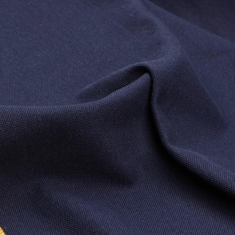 Gros plan sur le Tissu piqué uni au mètre de Longan Craft France, tissu coton-polyester bleu marine pour polos et chemises d'été, montrant son tissage subtilement texturé et un léger pli.