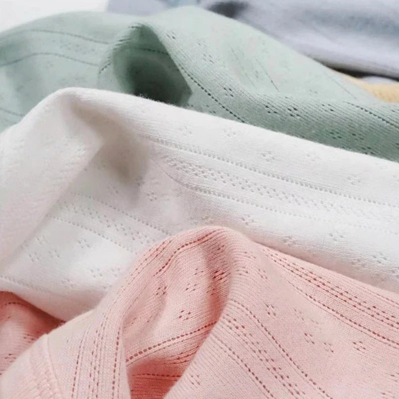 Gros plan sur la maille pointelle côtelée unie au mètre de Longan Craft France, un tissu en coton biologique doux et respirant, de couleur vert pastel, blanc et rose, idéal pour les vêtements de bébé grâce à sa texture délicatement côtelée et ses minuscules perforations.