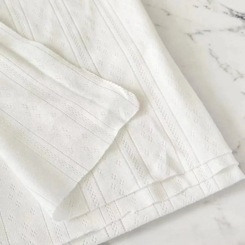 Gros plan sur Maille pointelle côtelée unie au mètre de Longan Craft France, un tissu pointelle en coton biologique doux et respirant, idéal pour vêtements bébé, avec motif subtil de rayures et losanges sur fond blanc marbré.