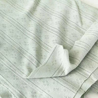 Gros plan sur la Maille pointelle côtelée unie au mètre de Longan Craft France, un tissu vert clair en coton biologique texturé avec de subtiles perforations en losange, idéal pour les vêtements bébé. Le tissu doux et respirant est légèrement plié et posé à plat.
