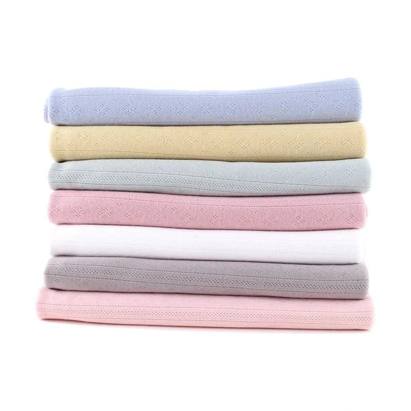 Une pile de sept serviettes pastel - bleu, jaune, vert, blanc, rose, gris et rose pâle - fabriquées en Maille pointelle côtelée unie au mètre par Longan Craft France en coton biologique doux est posée sur un fond blanc uni.