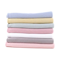Une pile de sept serviettes pastel - bleu, jaune, vert, blanc, rose, gris et rose pâle - fabriquées en Maille pointelle côtelée unie au mètre par Longan Craft France en coton biologique doux est posée sur un fond blanc uni.