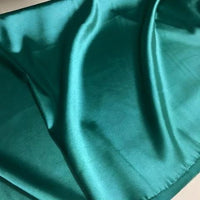 Un gros plan de Tissu satin polyester uni au mètre de Longan Craft France montre un tissu lisse et brillant de couleur vert sarcelle avec des plis doux - satin extensible idéal pour des vêtements ajustés et confortables.