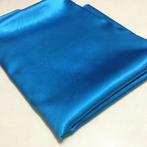 Un morceau soigneusement plié de Tissu satin polyester uni au mètre de Longan Craft France, d'un bleu brillant, est présenté sur une surface lisse et claire, idéale pour créer des vêtements ajustés, confortables et extensibles.