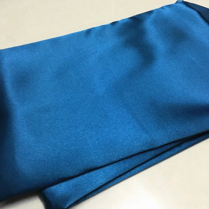 Un morceau de Tissu satin polyester uni au mètre, bleu et brillant, parfait pour des vêtements ajustés et confortables, de Longan Craft France, est étalé à plat, montrant sa texture lisse et légèrement extensible.