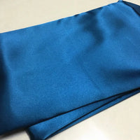 Un morceau de Tissu satin polyester uni au mètre, bleu et brillant, parfait pour des vêtements ajustés et confortables, de Longan Craft France, est étalé à plat, montrant sa texture lisse et légèrement extensible.