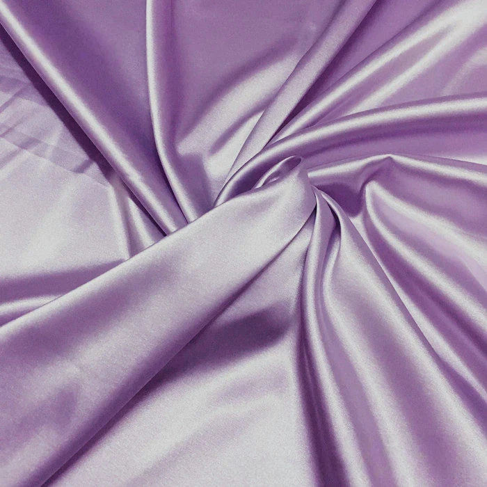 Un gros plan de Tissu satin polyester uni au mètre de Longan Craft France montre un satin violet clair à la texture douce et lisse et aux plis délicats, idéal pour créer des vêtements ajustés et confortables.
