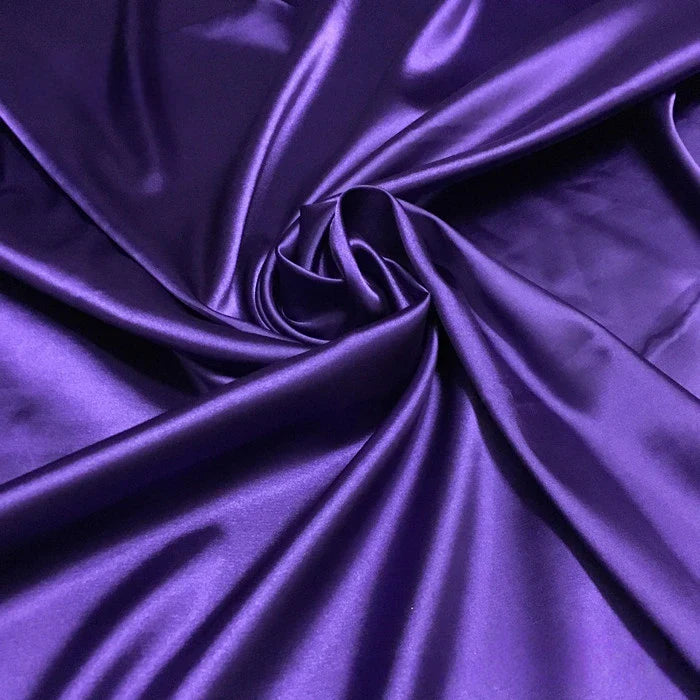 Le Tissu satin polyester uni au mètre de Longan Craft France est présenté dans un motif tourbillonnant, avec des plis souples qui reflètent la lumière et révèlent sa texture brillante - idéal pour les vêtements ajustés et confortables.