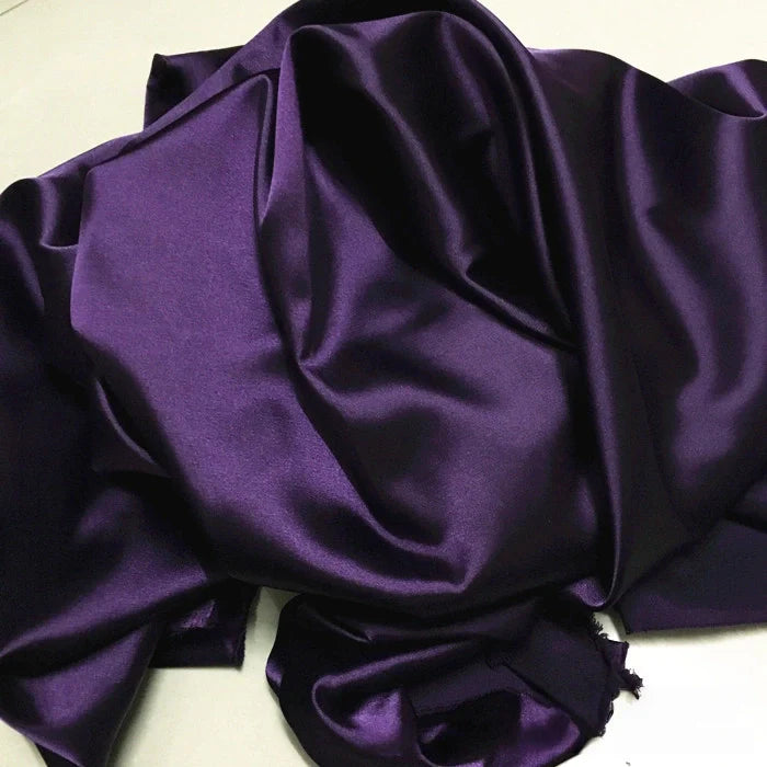 Le Tissu satin polyester uni au mètre de Longan Craft France est présenté sur une surface claire, mettant en valeur sa texture lisse et brillante et ses plis élégants, idéaux pour des vêtements confortables et ajustés.
