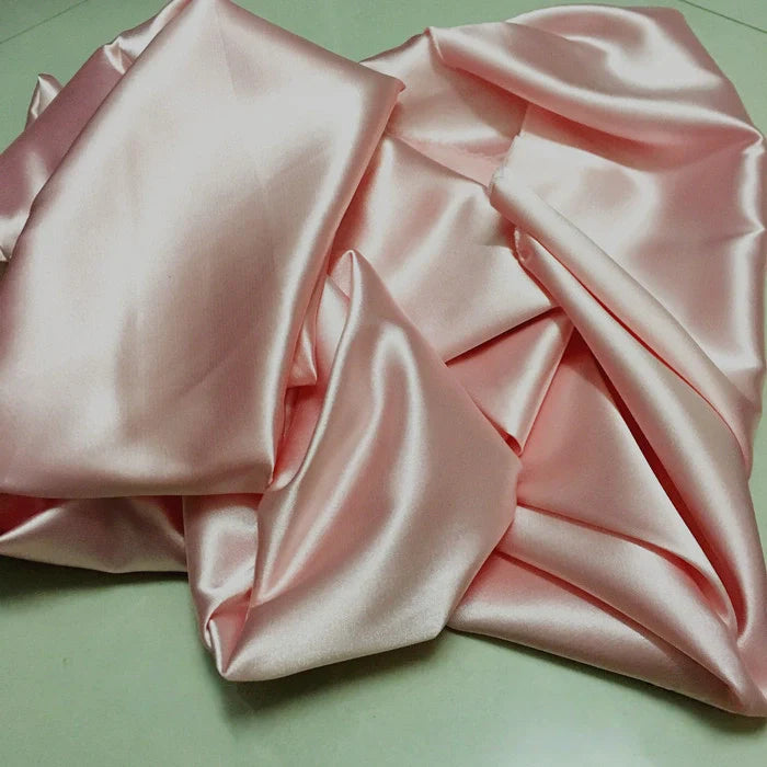 Une pile de Tissu satin polyester uni au mètre de Longan Craft France, avec une surface lisse et brillante, est librement rassemblée - idéale comme satin extensible pour des vêtements ajustés et confortables.