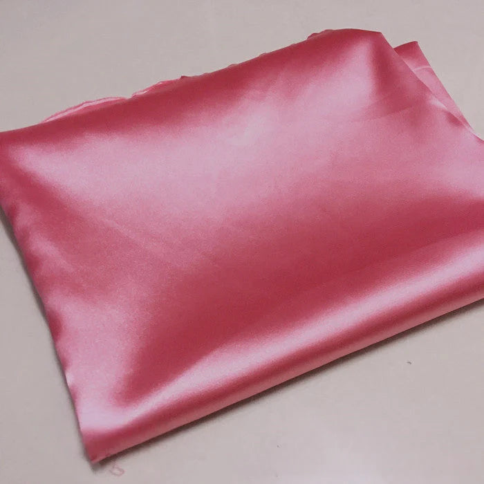 Un morceau plié de Tissu satin polyester rose brillant uni au mètre de Longan Craft France repose sur une surface légère. Ce tissu satin extensible est parfait pour créer des vêtements ajustés et confortables.