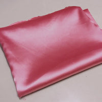Un morceau plié de Tissu satin polyester rose brillant uni au mètre de Longan Craft France repose sur une surface légère. Ce tissu satin extensible est parfait pour créer des vêtements ajustés et confortables.