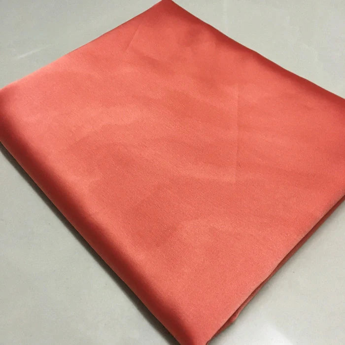 Tissu satin polyester uni au mètre plié de Longan Craft France, tissu satin rouge extensible pour vêtements confortables et ajustés, présenté sur une surface blanche.