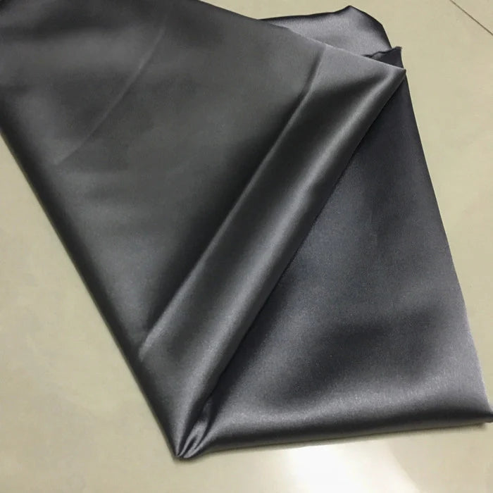 Une longueur de tissu satin polyester uni au mètre de Longan Craft France est pliée sur une surface légère. Sa finition extensible et brillante est lisse et douce, parfaite pour créer des vêtements ajustés et confortables.