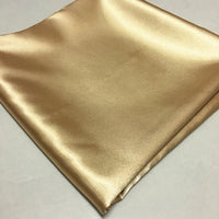 Un tissu polyester satiné brillant et doré de Longan Craft France, soigneusement plié, est présenté sur une surface claire - un matériau extensible idéal pour des vêtements confortables et ajustés.