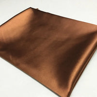 Un morceau soigneusement plié de Tissu satin polyester brun brillant uni au mètre de Longan Craft France, idéal pour créer des vêtements confortables et ajustés, est présenté sur une surface blanche.
