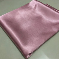 A piece of Tissu satin polyester uni au mètre de Longan Craft France, extensible, rose clair, est posé sur une surface lisse, montrant sa texture brillante et douce-idéal pour des vêtements ajustés et confortables.