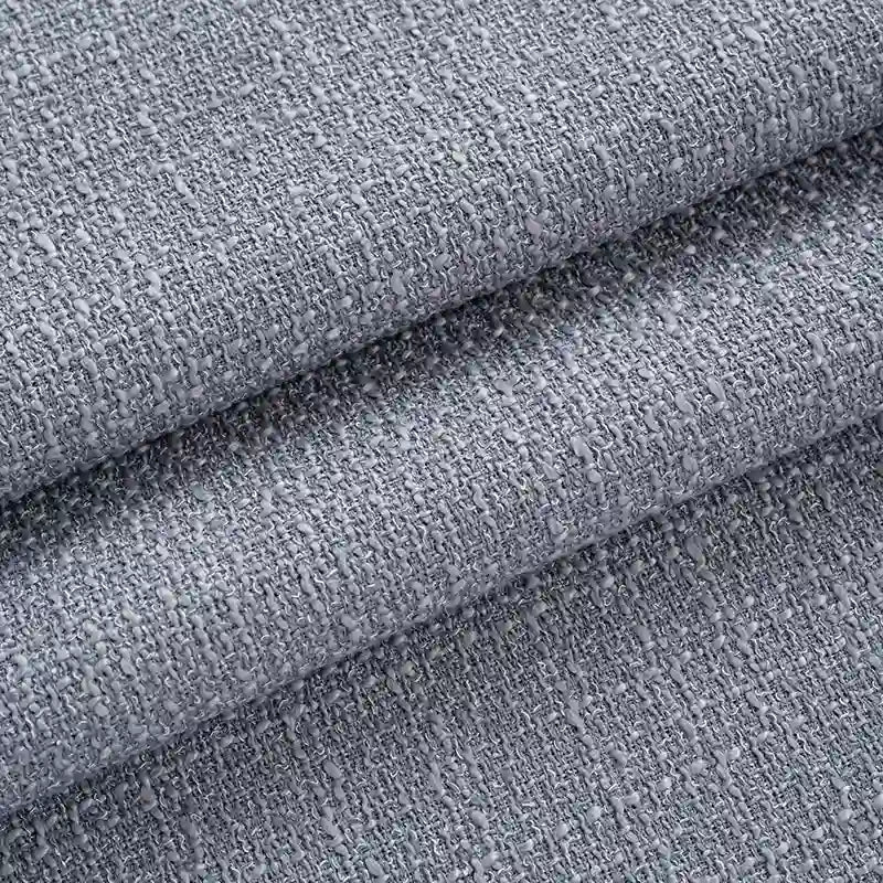 Gros plan sur le pliage de Tissu tweed uni au mètre de Longan Craft France, un tissu tweed gris en polyester à la surface texturée et tissée, doux et épais, parfait pour les vêtements ou les costumes chics.